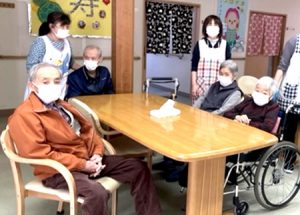 食事風景。スタッフと入居者が長テーブルで一緒に食事をしている情景。